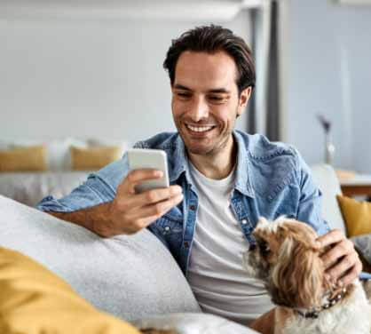 Man patting dog and using smartphone