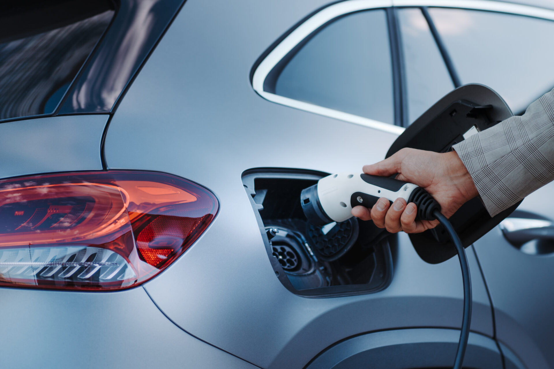 Alt text: Close-up of a hand plugging a charging cable into an electric vehicle's charging port
