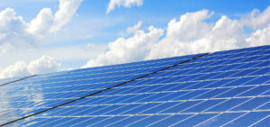 Rows of solar panels on a large commercial rooftop against a blue sky with clouds